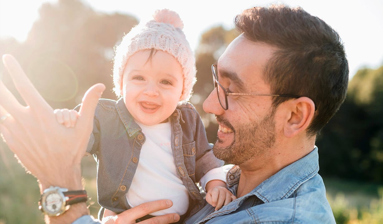 A cheerful father holding his smiling baby outside in the sunlight